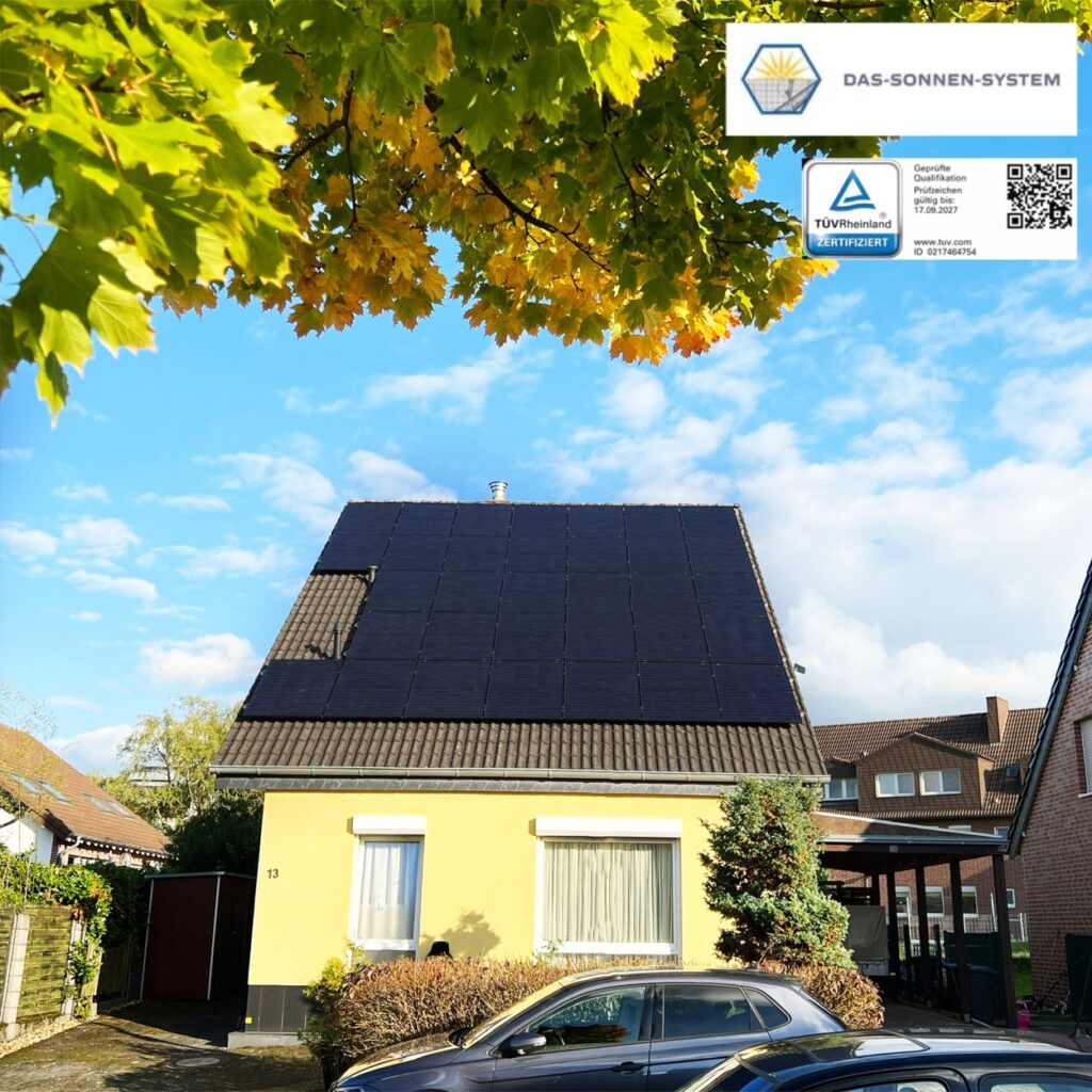 Gelbes Haus mit Solaranlage, blauer Himmel, Herbstblätter; vorderer Hof mit geparktem Auto.