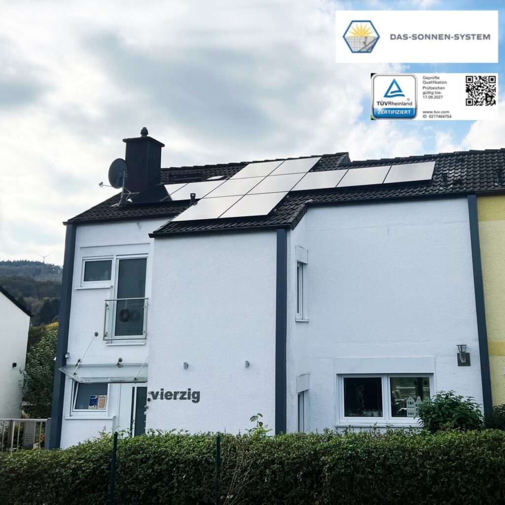 Ein weißes Haus mit Solarmodulen auf dem Dach und einem TÜV-Zertifikatschild.