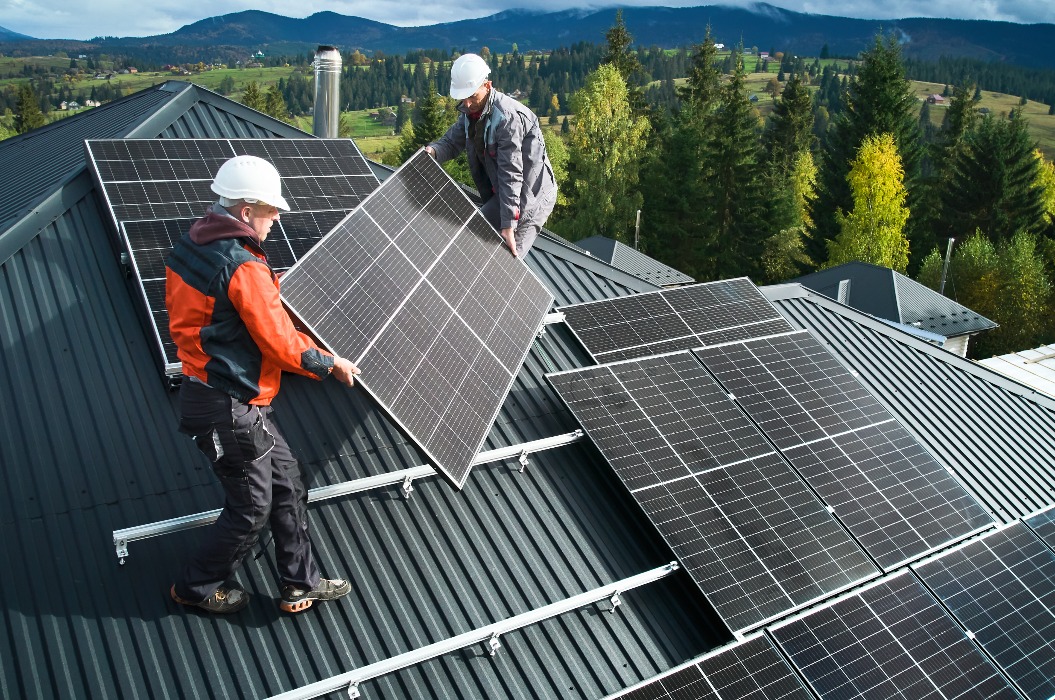 Arbeiter bauen Solarmodulsystem auf dem Dach eines Hauses. Männer Techniker in Helmen tragen photovoltaische Solarmodule im Freien. Konzept der alternativen und erneuerbaren Energie.